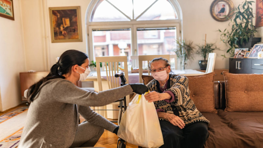 Worker delivers bag of groceries to older woman at home