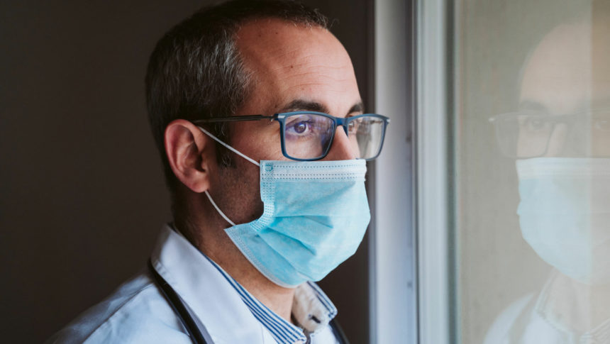 man wearing medical mask and looking out a window