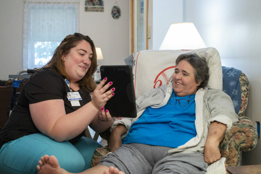 Image of caregiver showing tablet to homebound person on couch