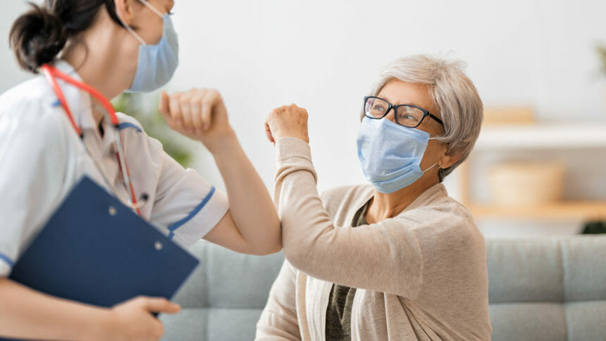 Older woman and nurse wearing facemasks bump arms