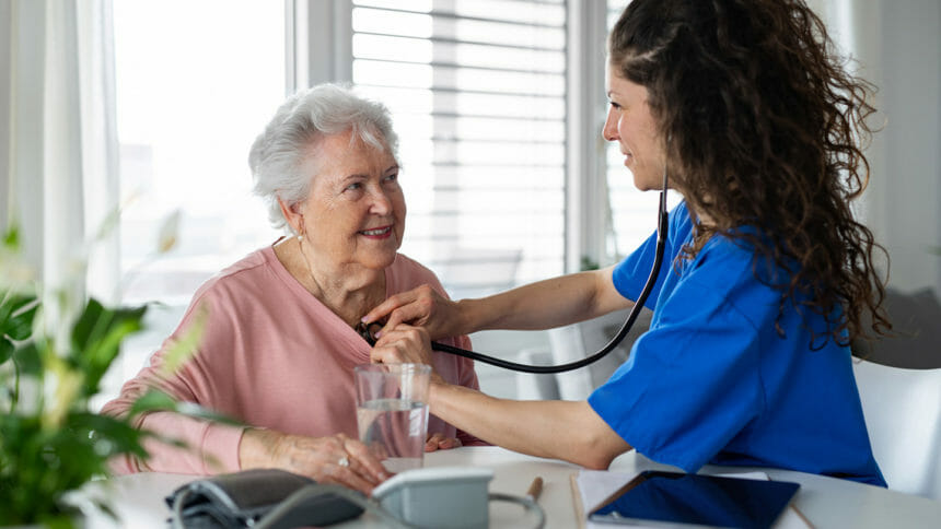 Nurse in blue scrubs checks older woman's heart with stethoscope