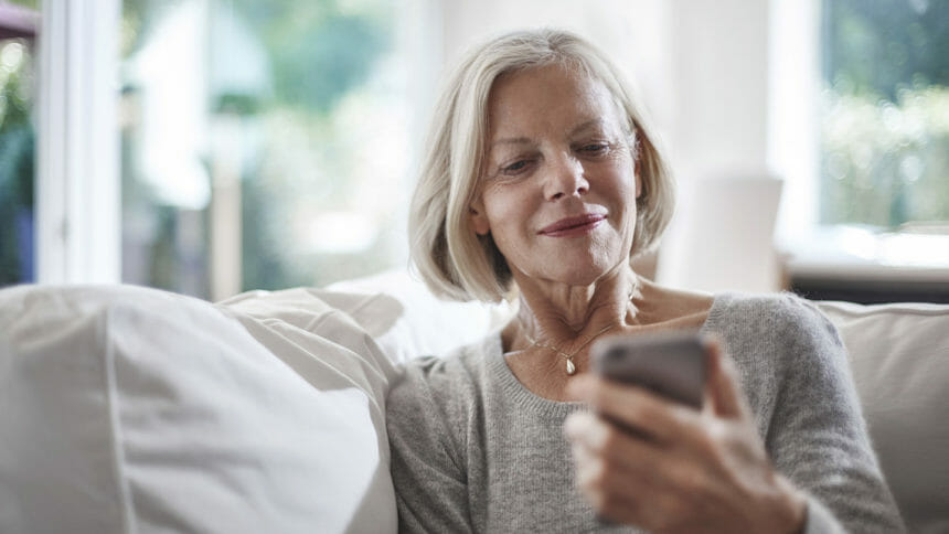 Vibrant senior looks at cell phone while relaxing on couch