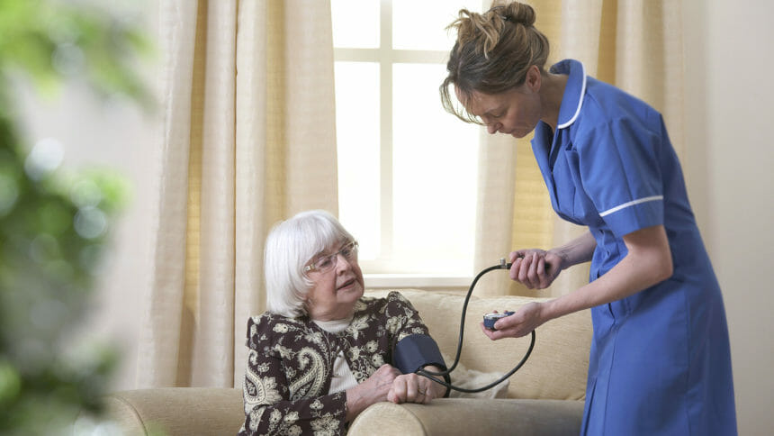 Healthcare provider takes blood pressure of senior sitting on couch