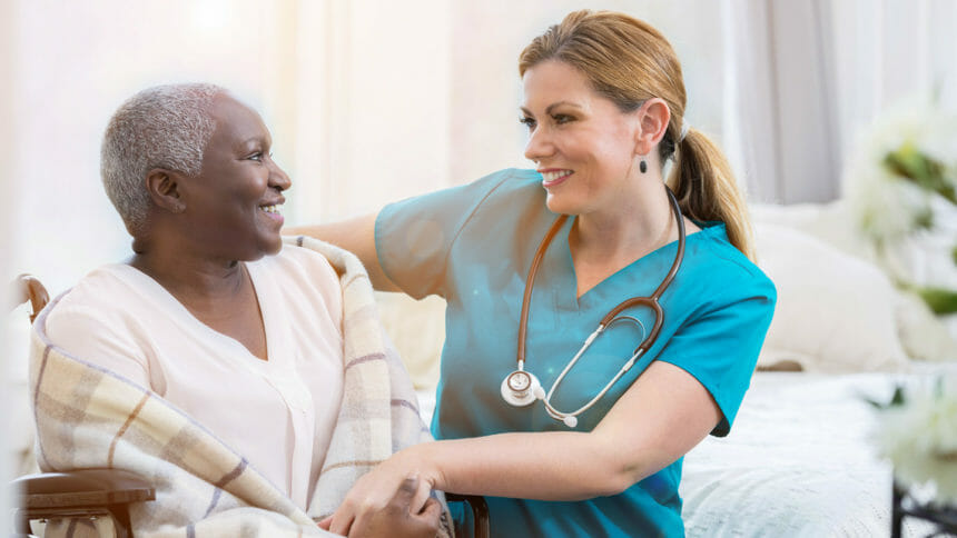 Smiling home health nurse holds hand of content woman in wheelchair