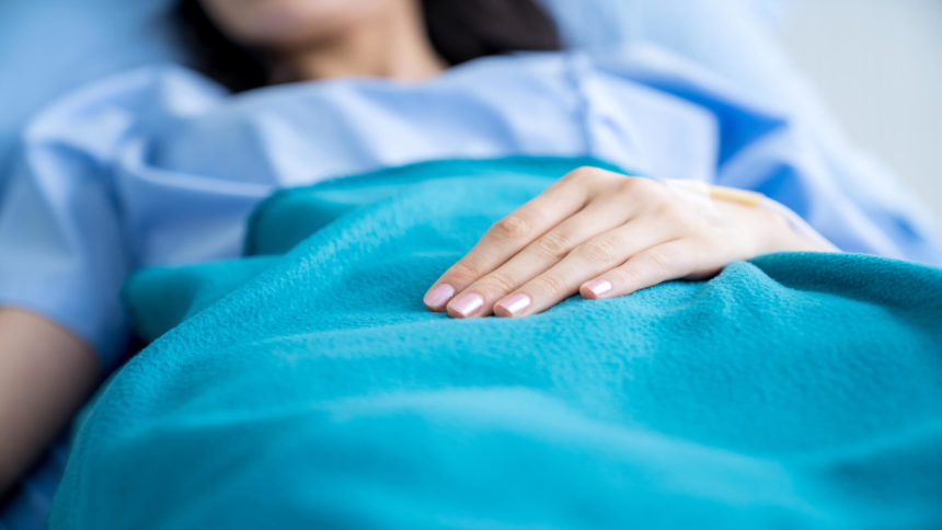 Woman wearing blue gown lies in bed with her hand resting on a blanket