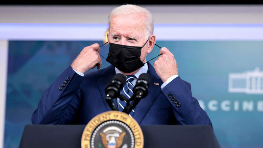 President Biden removes a face mask before speaking at the podium.