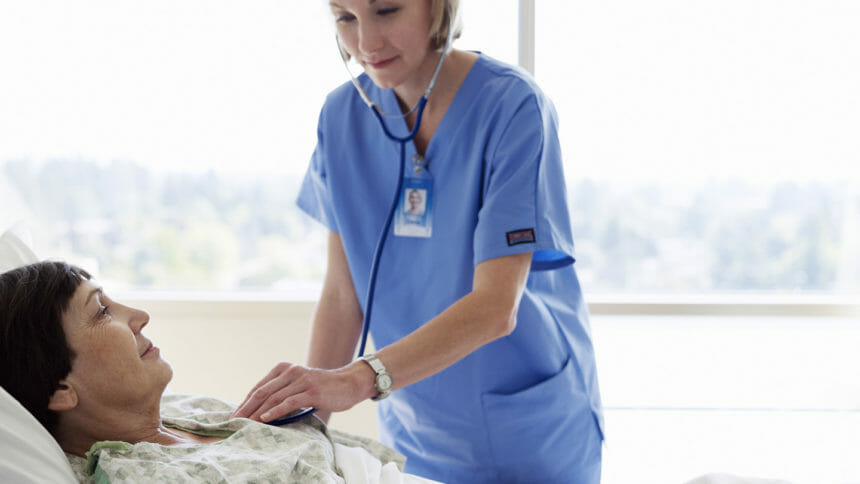 Healthcare professional wearing stethoscope monitors heart of woman lying in bed