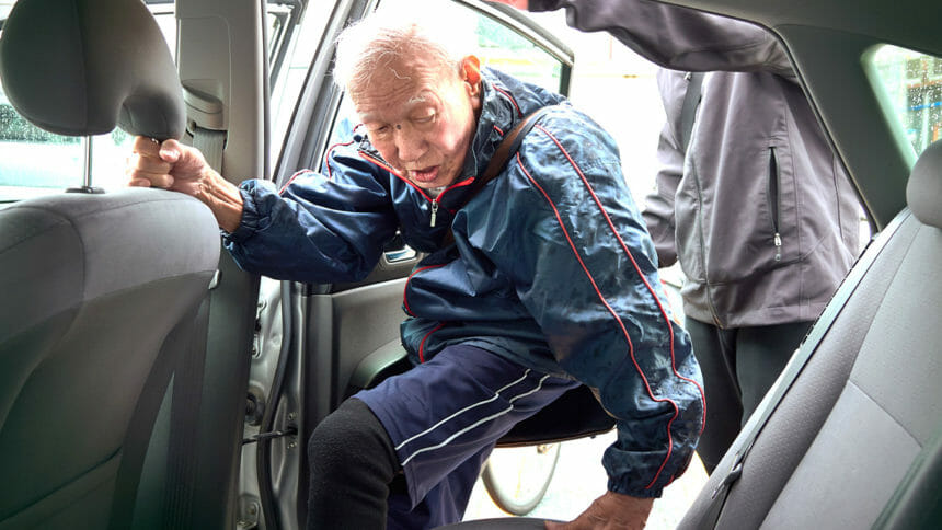 Older man wearing wind breaker gets into car