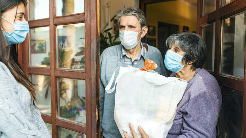 Senior couple receives groceries from young woman in face mask