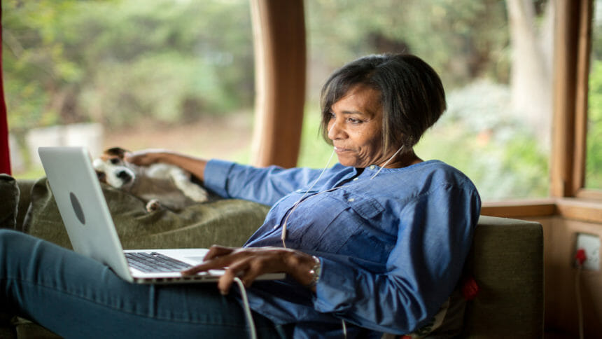 Middle-aged African-American woman looks at computer while sitting on couch at home
