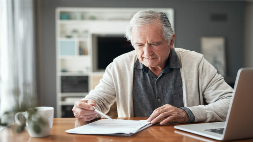 Older man looks at some documents next to his computer