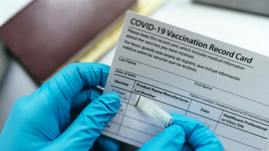 Gloved hands hold a COVID-19 vaccination card