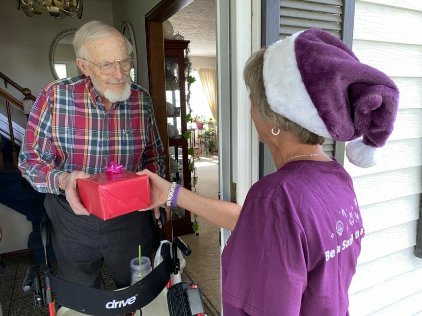 Woman wearing Santa hat gives a gift to a senior man.
