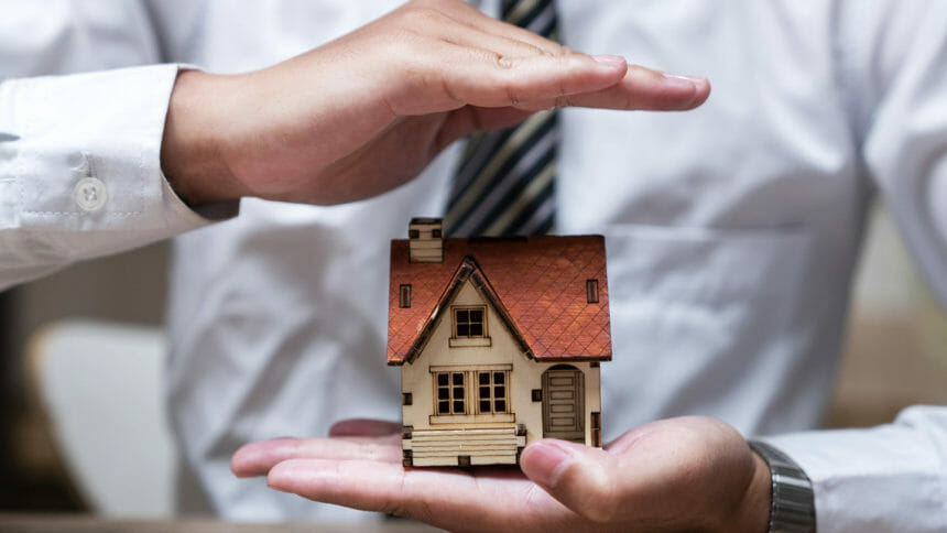 A businessman's hand holds a model of a house and indicates with the other hand that the house will grow