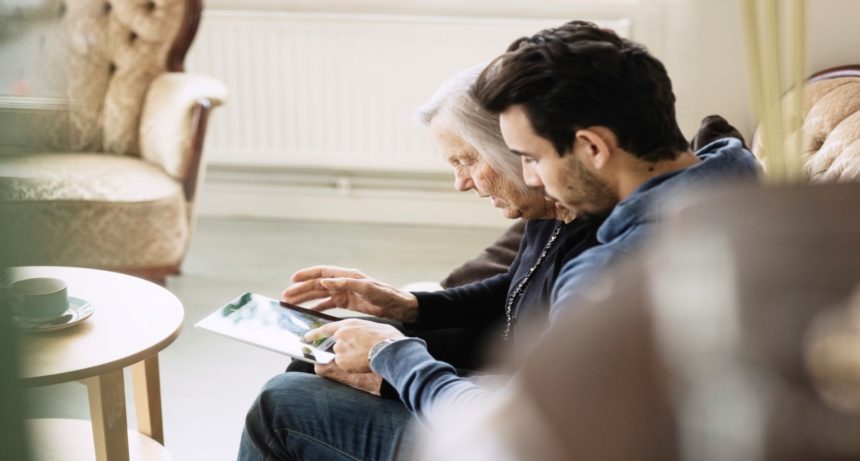 Younger man and older woman sitting close look at tablet together