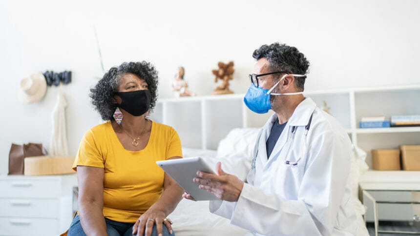 Doctor using digital tablet visiting senior patient at home - wearing face mask