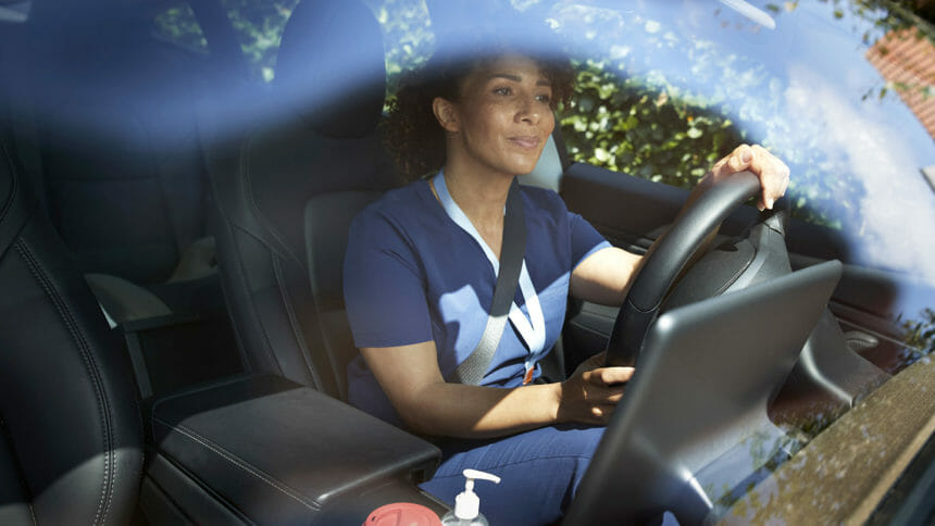 Smiling female healthcare worker driving car seen through windshield