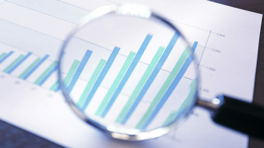 A close up of a magnifying glass rests on top of a bar graph that shows growing sales or increasing performance over a quarterly basis.