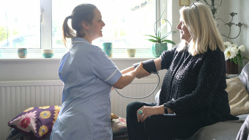 nurse checking blood pressure of senior female patient in lounge room