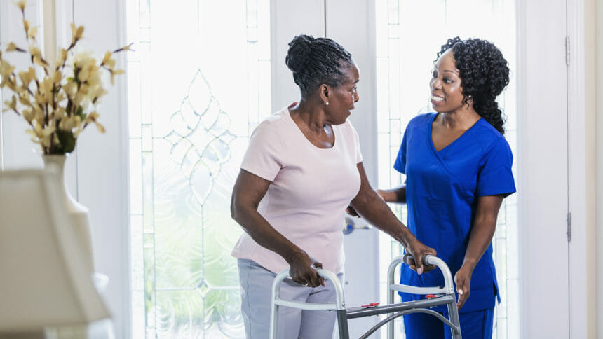 A healthcare worker visiting a senior African-American woman at home, helping her use a mobility walker