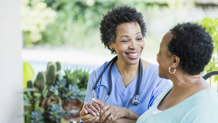 A home healthcare worker, a mature African-American woman in her 50s, visiting a patient on a back yard patio.