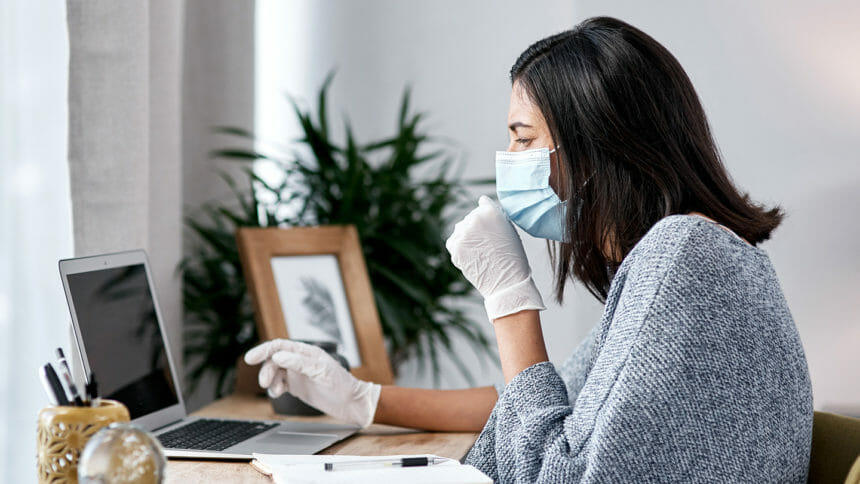 Shot of a masked young woman coughing while working from home