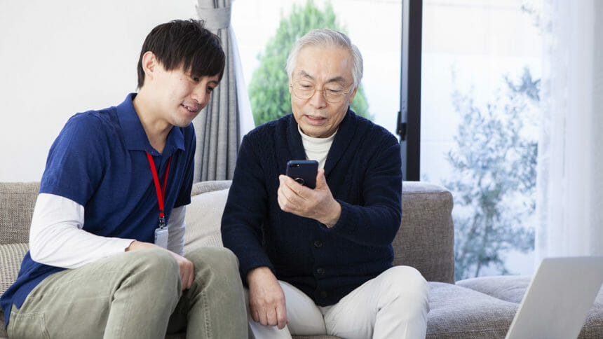 Senior man looks at cell phone as young caregiver looks on
