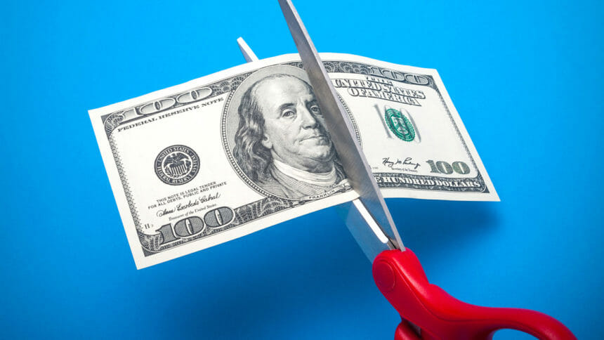 100 dollar bill being cut with scissors isolated on a blue background
