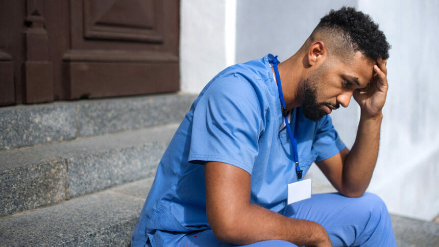 Overworked male doctor or male nurse sitting in front of the building having headache