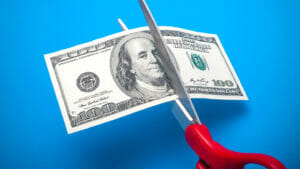 100 dollar bill being cut with scissors isolated on a blue background