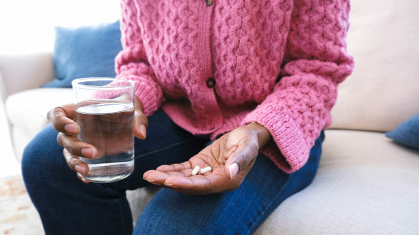 woman sitting on couch holding medication/supplements and glass of water