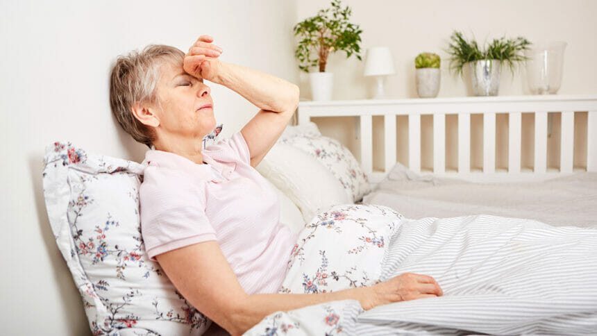 Senior woman with disease lie on bed with headache