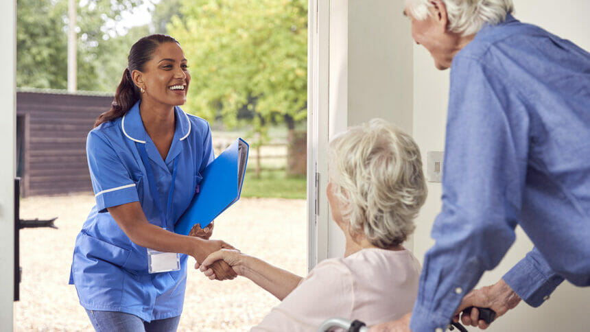 Female caregiver greets older couple at door