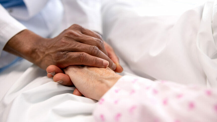Close-up on a doctor holding the hand of a sick woman in bed at the hospital - healthcare and medicine and hospice