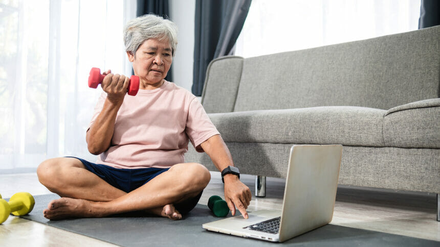 Superaging senior exercising while working on laptop