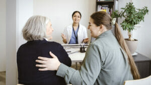 Family caregivers with hand on back of mother sitting in clinic photographed from behind