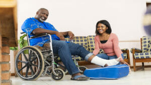 Portrait of young woman helping senior man in wheelchair with injured foot