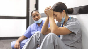 RNs experiencing the workforce shortage sits sadly on the ground as another caregiver seeks to console her.