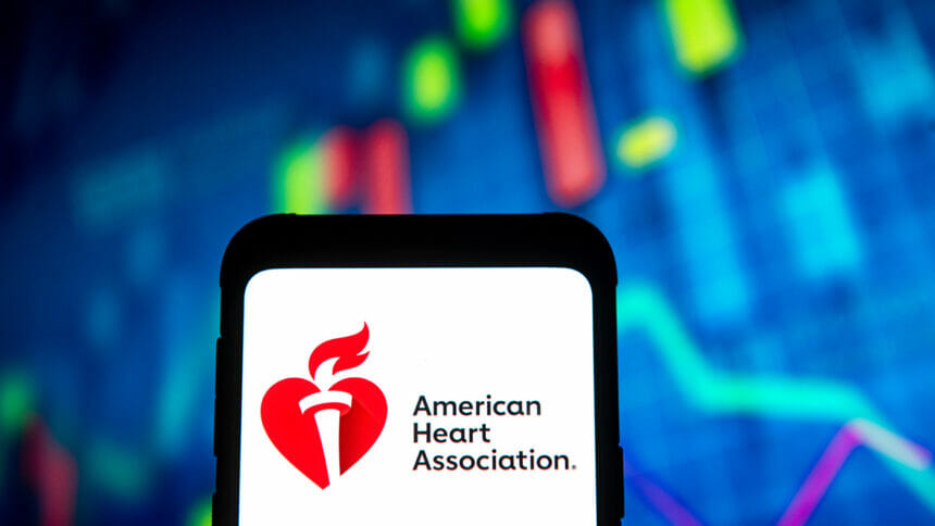 The American Heart Association logo on a phone in front of stock graphs