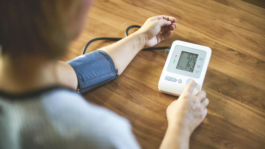 A person performs home blood pressure monitoring with a small home monitor affixed to their arm