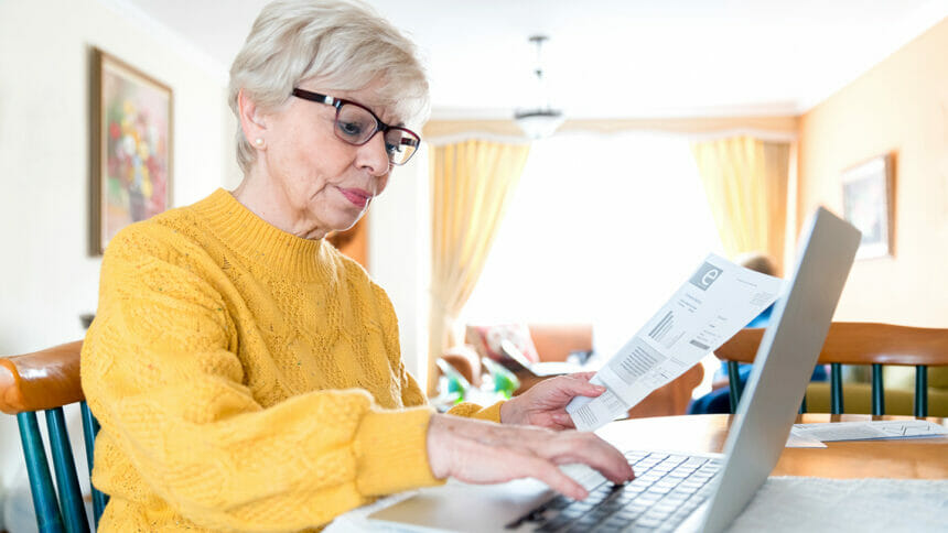 Portrait of senior woman paying her utility bills online at home using a laptop computer - elders using technology concepts