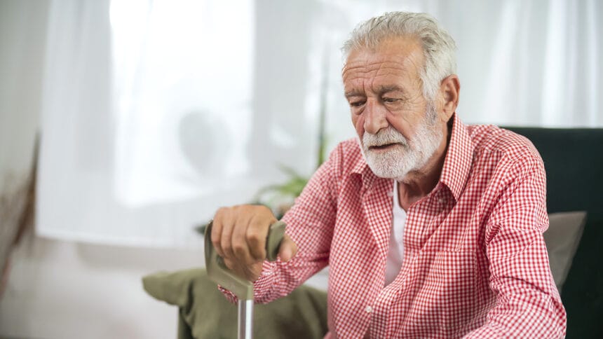Thoughtful elderly man sitting alone at home with his walking cane