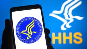 UKRAINE - 2021/11/05: In this photo illustration, United States Department of Health and Human Services (HHS) seal logo is seen displayed on a smartphone in a hand and in the background. (Photo Illustration by Pavlo Gonchar/SOPA Images/LightRocket via Getty Images)